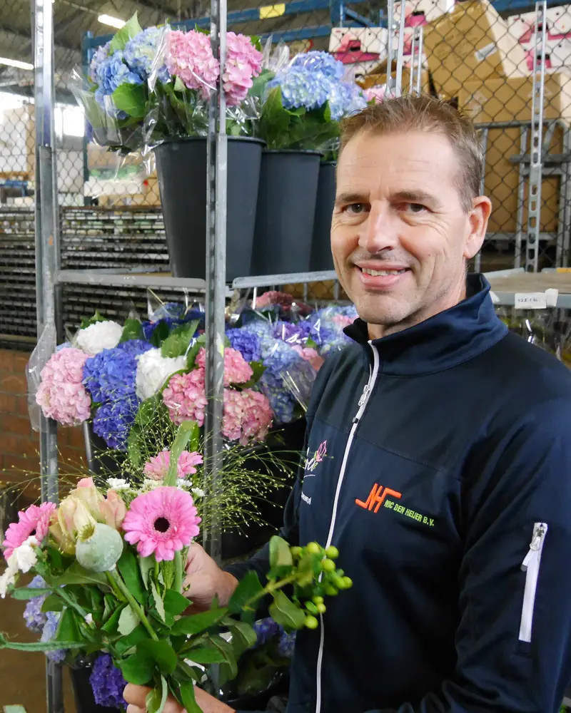 Ron Hogenboom, directeur van Nic. den Heijer, met een boeket roze en witte bloemen in de bedrijfshal